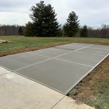 Freshly poured concrete slab in a grassy area with surrounding trees. Ideal for outdoor projects.