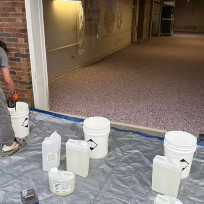 Person applying resin on a floor with paint buckets and protective covering in a garage space.