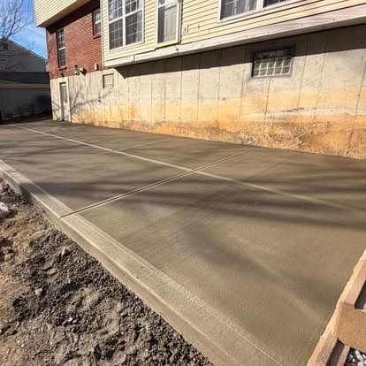 Freshly poured concrete slab for driveway installation next to a residential building.