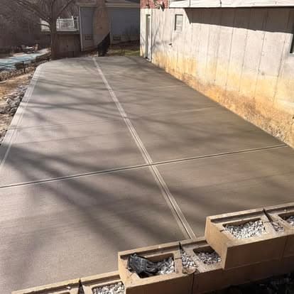 Freshly poured concrete driveway with visible expansion joints and shadows from nearby trees.