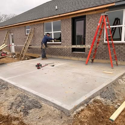 Construction worker measuring exterior brick walls of a house with a red ladder nearby.