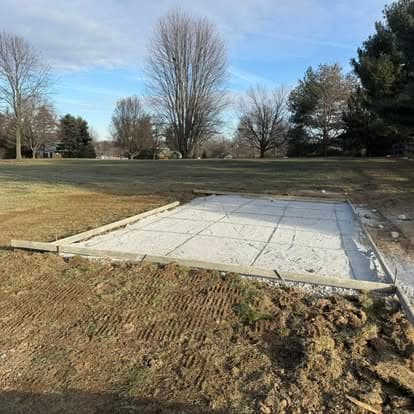 Concrete foundation slab on a grassy site, surrounded by trees and clear sky.