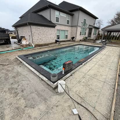 In-ground pool installation beside a modern house under construction.