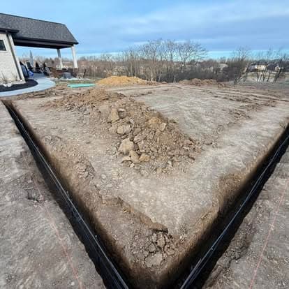 Excavated foundation site with dirt mounds and marked boundaries for construction project.