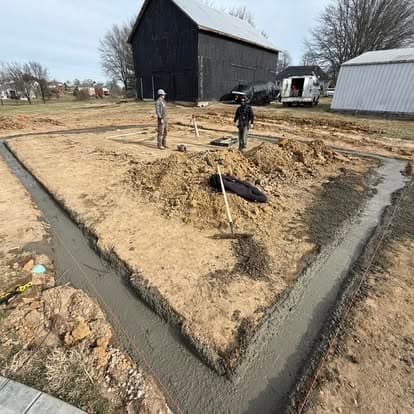 Construction workers laying a concrete foundation on a building site near a barn.