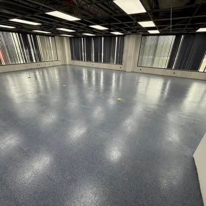 Empty commercial space with blue flooring and large windows covered by vertical blinds.