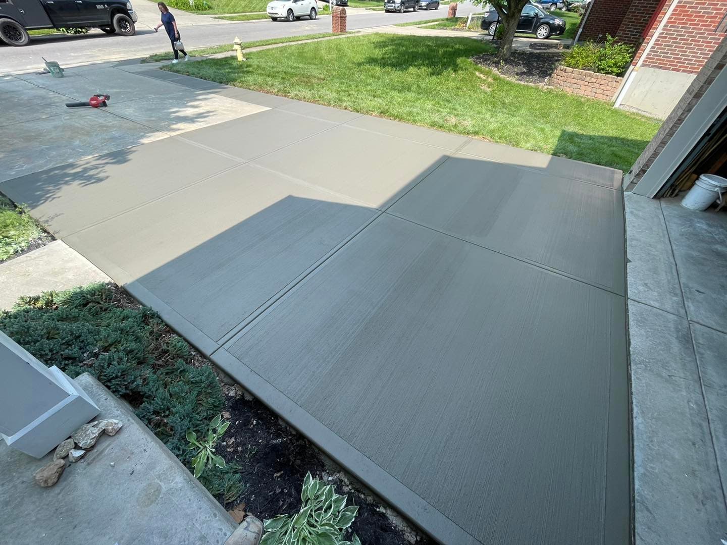 Freshly poured concrete driveway with smooth finish, surrounded by grass and landscaping.