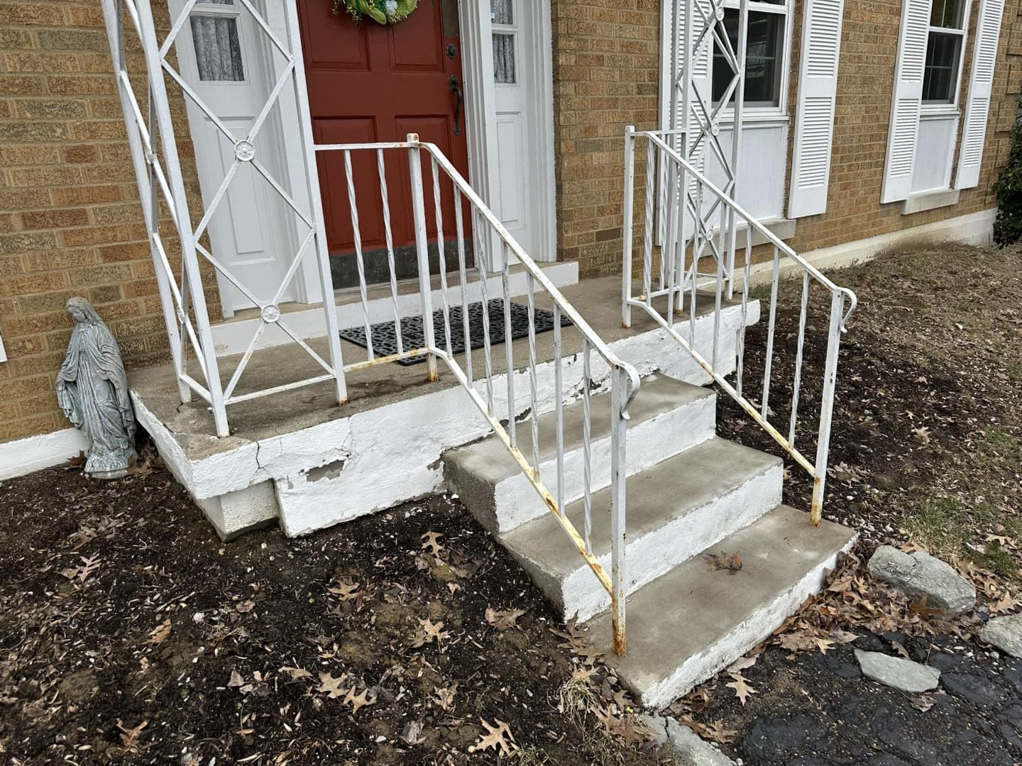 Weathered concrete steps with white railings, leading to a front door in a brick home.